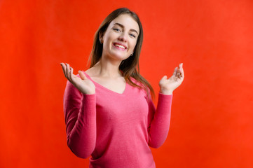Fototapeta premium Photo on a red background of a pretty smiling woman in a pink sweater showing joy