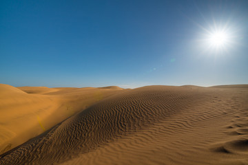 Desert landscape. Beautiful golden sand dunes, blue sky, sun and sun rays. Gran Canaria desert. Maspalomas, South Gran Canaria, Spain