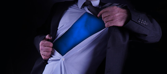Superhero, young businessman tearing his shirt off isolated on dark background with copy space