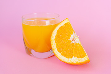 Orange juice and piece of orange with pink background.