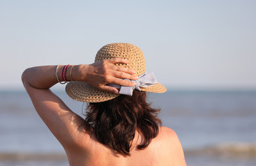 woman waiting with hand on the straw hat in summer