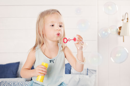 Portrait of funny little girl blowing bubbles at home