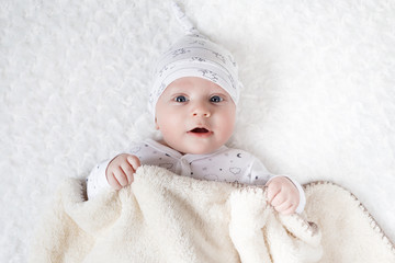 four-month-old white boy with blue eyes lies on a white blanket and take cover with him