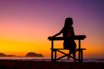 Fototapeta na wymiar Beautiful silhouette of a brunette looking right in a chair on the beach on a sunset looking at the sea