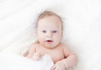 four-month-old white boy with blue eyes lies on a white blanket and take cover with him