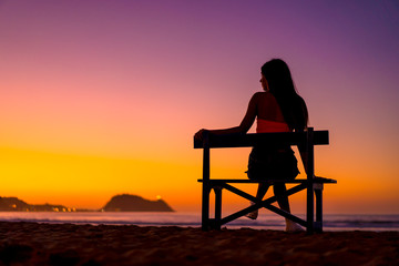 Fototapeta na wymiar Beautiful silhouette of a brunette looking left in a chair on the beach on a sunset looking at the sea