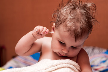 Caucasian baby picking his ear with cotton swab, child after bathing, disheveled hair