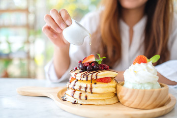 A beautiful woman pouring honey into a piece of mixed berries pancakes with ice cream and whipped cream
