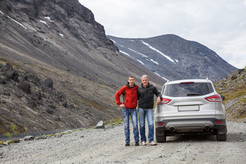 Senior father and adult son traveling together by car in mountains, off road driving on dirt road