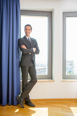 Handsome young businessman wearing suit posing in hotel room by the window