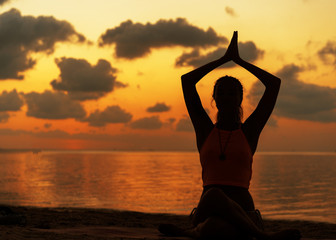 girl doing yoga on the beach at sunset