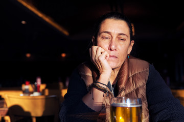 Unhappy, depressed and lonely middle age woman sitting at the bar with a beer glass