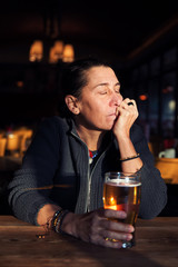 Unhappy, depressed and lonely middle age woman sitting at the bar with a beer glass