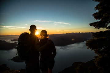 COUPLE STANDING on the top of mountain overlooking islands during sunset in beautiful British Columbia Vancouver Canada after hike in forest 