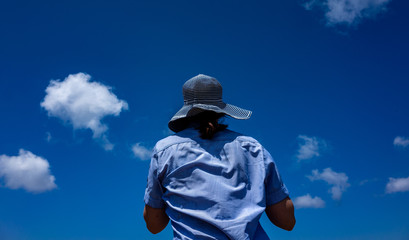 Obraz premium Girl in a wide-brimmed striped hat on a background of blue sky with small clouds