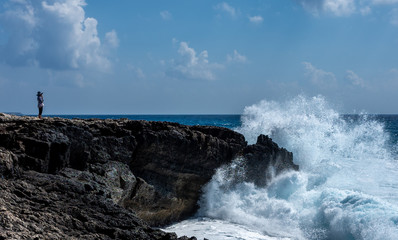 A girl on the beach watches the waves breaking on the rocky shore of the Mediterranean Sea on the Akamas Peninsula in the northwest of the island of Cyprus.