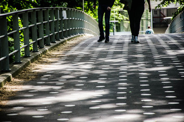 Two pair of legs walking over a bridge with sunlight making a pettern with shadows. .