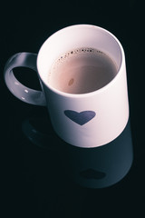 Heart shape painted on a white coffee morning mug on a black surface background