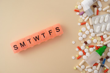 Daily pill box with medications and nutritional supplements. Vitamins, pills blister packs medical bottle, asthma inhaler on yellow background. Medical, pharmacy and healthcare concept.