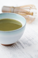 Green matcha tea and bamboo whisk on bright wooden background. Close up.	