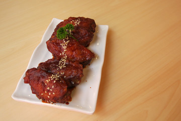 chicken wings with Korea sauce and white sesame in the white plate placing on the brown wooden table