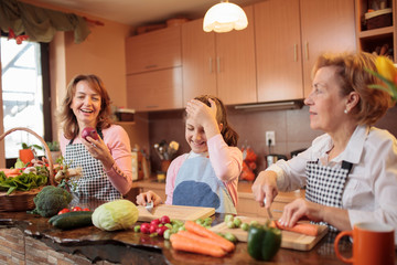Young caucasian teenage girl preparing food, helping her mother and grandmother by cutting fresh vegetables in home kitchen