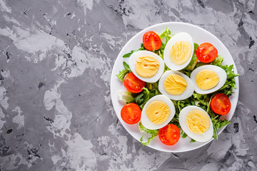 salad with boiled chicken eggs and cherry tomatoes on a stone background