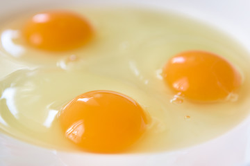 Three fresh eggs crushed on a white plate