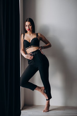 a young girl with dark hair, brown eyes and bright red lips poses in a Studio in black underwear and black trousers