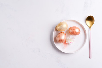 Greeting card with handmade painted bright eggs on a plate and golden spoon on a light grey marble background.