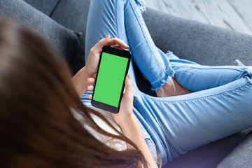 Woman takes a rest on sofa with a smartphone, view from above. Clipping path included.
