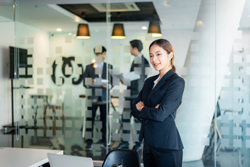 Portrait of young asian businesswoman standing at her office. background of businessman.