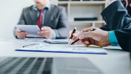 Business people gather to analyze marketing and investment information and using pen pointing to financial data chart at meeting.