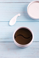 Cosmetics collagen brown patches in a plastic jar for skin around the eyes on a light blue wooden background.
