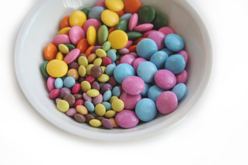 Chocolate candies with coloful glazes in a white bowl isolated on white background