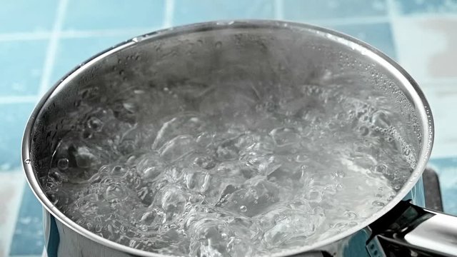 The pan of boiling clean water in close-up on the stove, after removing the lid