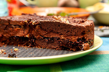 Simple sweet tasty homemade fresh flat brown chocholate cake with filling on a green plate on the table. Cross section, intersection, cake cut in two, macro, closeup, food photography background