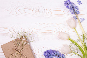 A gift box wrapped in craft paper and blue hyacinth flowers, white tulips on a white table top. Flat lay. Copy space for text