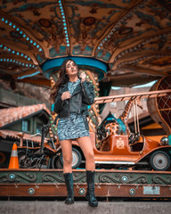 Fototapeta na wymiar Street style, sexy Caucasian brunette in a carousel at the fair with short skirt and a leather jacket