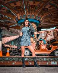 Fototapeta na wymiar A sexy Caucasian brunette in a carousel at the fair with a short skirt and a leather jacket