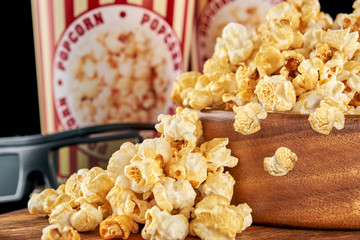 Popcorn flakes in a wooden bowl and paper cups on a dark background close-up.