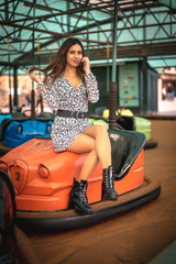 Lifestyle, a young Caucasian girl with long hair sitting in an orange crashed car with black boots at the village fair