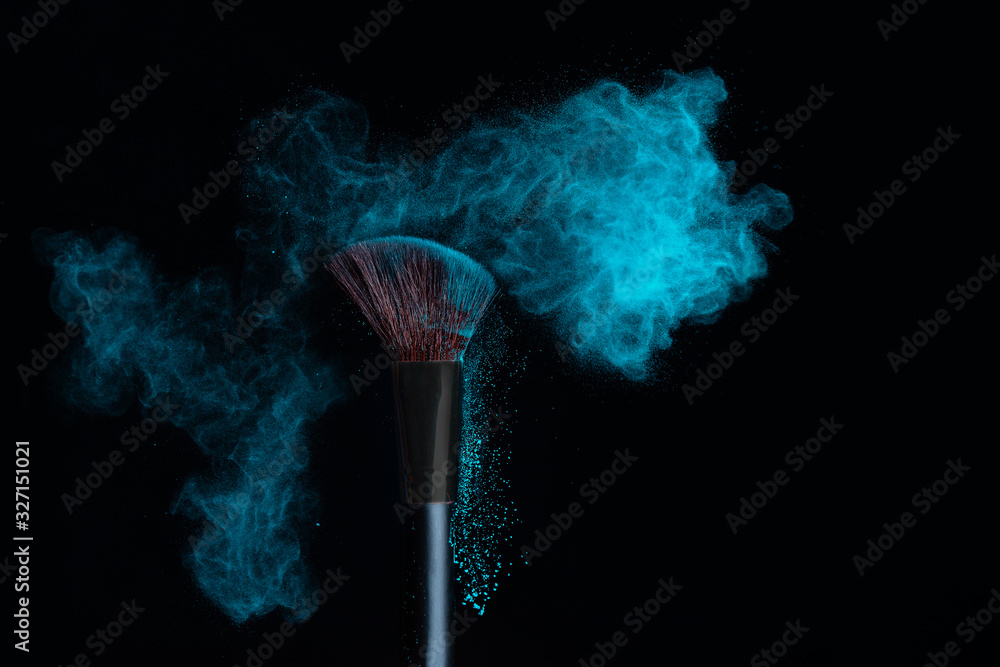 Wall mural Make-up brush with blue powder explosion isolated on a black background