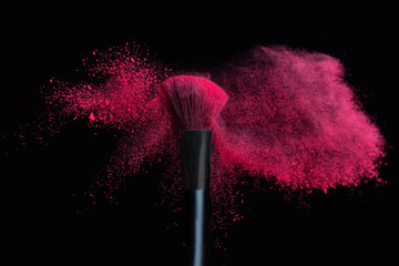 Make-up brush with pink powder explosion isolated on a black background