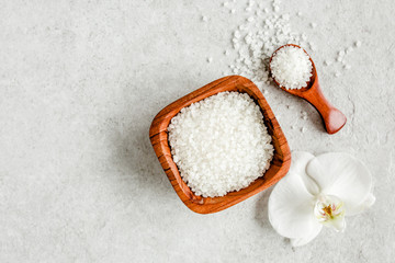 Salt in wooden bowl with scoop on gray stone table. Sea salt flat lay, top view. 