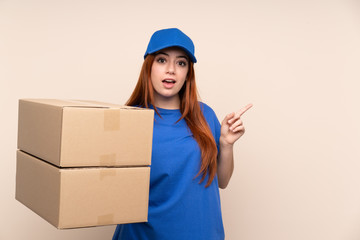 Young teenager delivery girl over isolated background surprised and pointing finger to the side