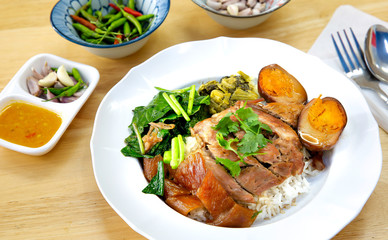 Stewed leg pork without fat in white dish and sour chili sauce in glass with fresh chili and garlic in white bowl on brown wooden table