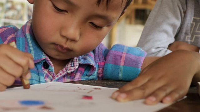 An Asian boy is drawing and coloring with fun.