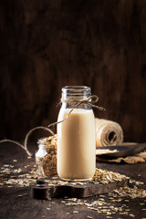 Oat flakes milk, non dairy alternative plant based drink in glass, wooden rustic kitchen table, copy space