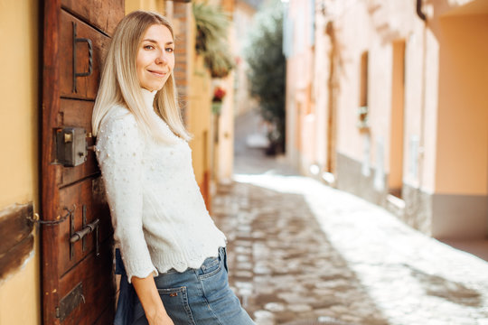 Fototapeta Beautiful happy smiling blonde hair woman posing outdoors leaning on the old door - discovering Italian streets